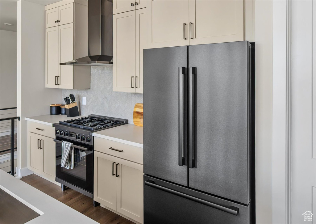 Kitchen with high end fridge, wall chimney exhaust hood, black gas range, light countertops, and dark wood-style floors