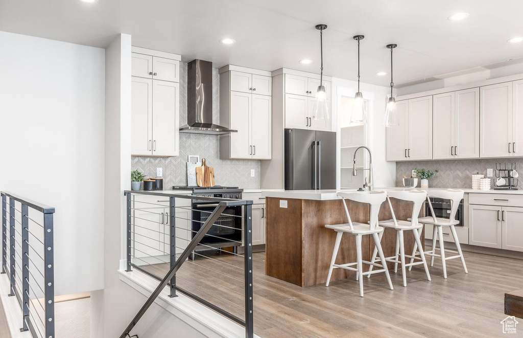 Kitchen with wall chimney range hood, high end refrigerator, decorative backsplash, a kitchen breakfast bar, and recessed lighting
