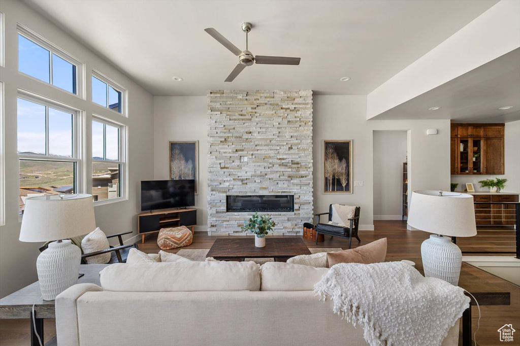 Living area with ceiling fan, a stone fireplace, wood finished floors, baseboard heating, and baseboards