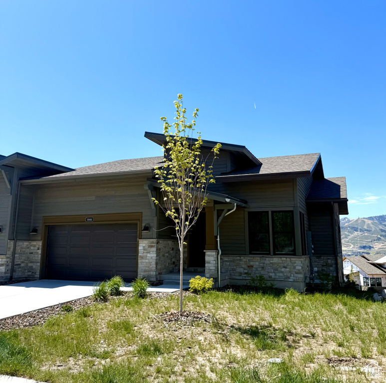 View of front of house with an attached garage, stone siding, concrete driveway, a mountain view, and roof with shingles