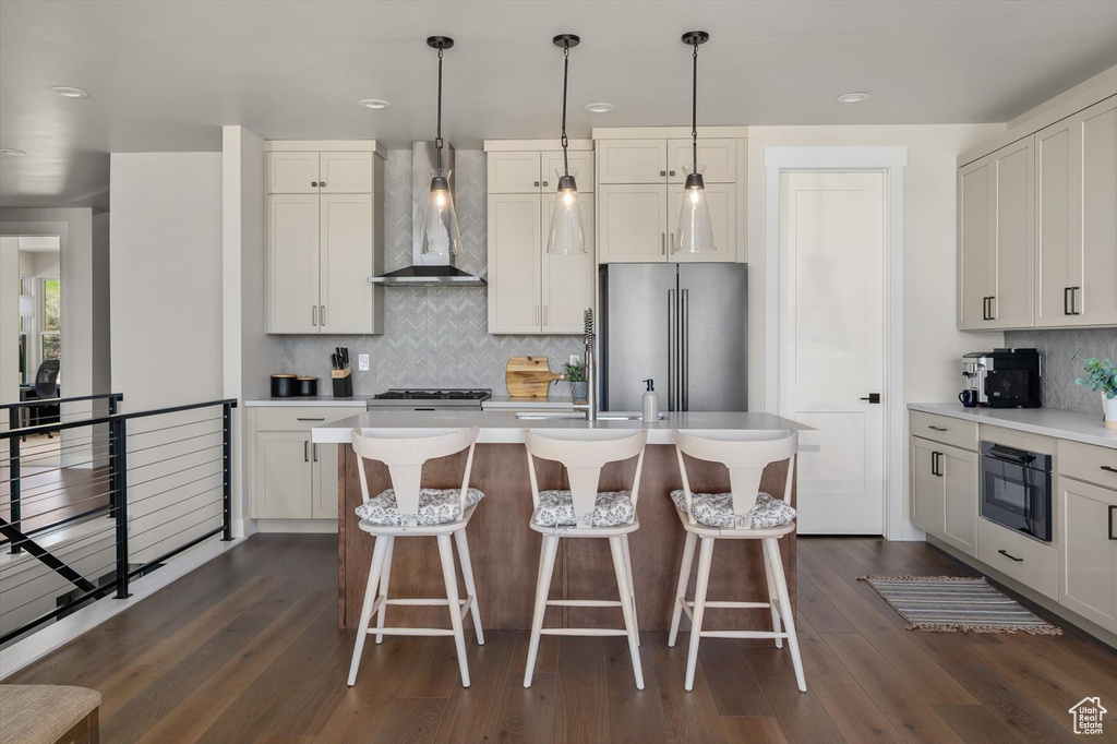 Kitchen featuring wall chimney exhaust hood, freestanding refrigerator, tasteful backsplash, light countertops, and dark wood-style floors