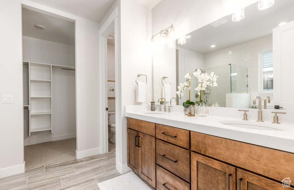 Full bath featuring a shower stall, double vanity, toilet, a spacious closet, and baseboards
