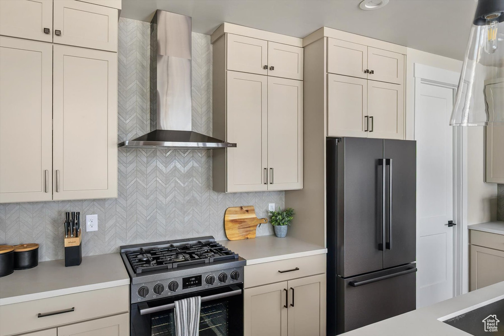 Kitchen featuring wall chimney exhaust hood, high end refrigerator, range with gas stovetop, and light countertops