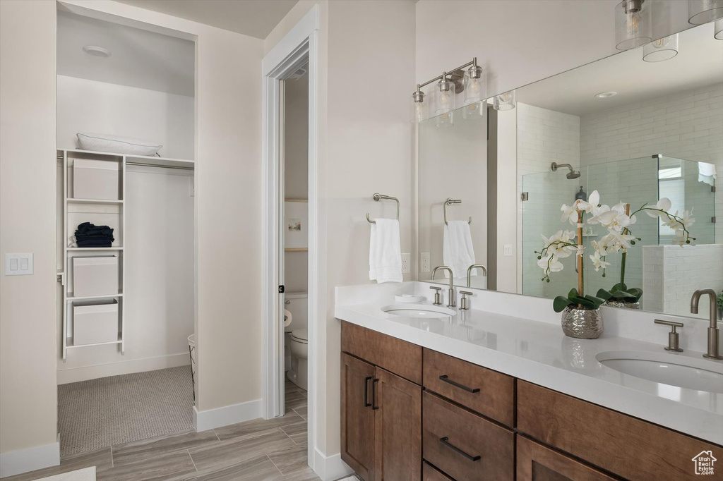 Bathroom with toilet, a shower stall, double vanity, wood finish floors, and baseboards