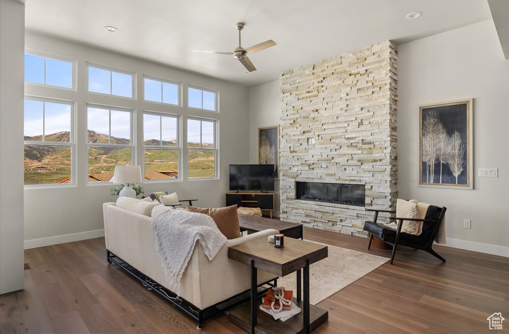 Living room featuring baseboards, a ceiling fan, wood finished floors, a stone fireplace, and recessed lighting
