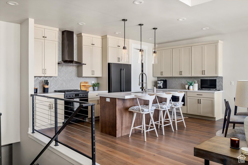 Kitchen featuring wall chimney exhaust hood, high quality fridge, gas stove, a kitchen island with sink, and recessed lighting