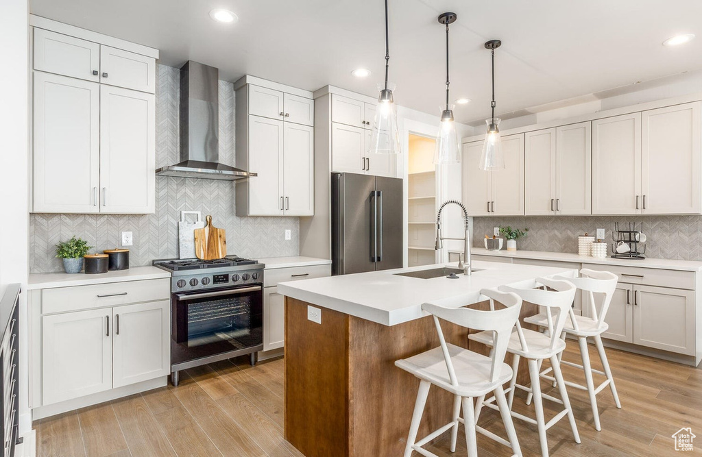 Kitchen with wall chimney range hood, appliances with stainless steel finishes, a sink, light wood finished floors, and backsplash