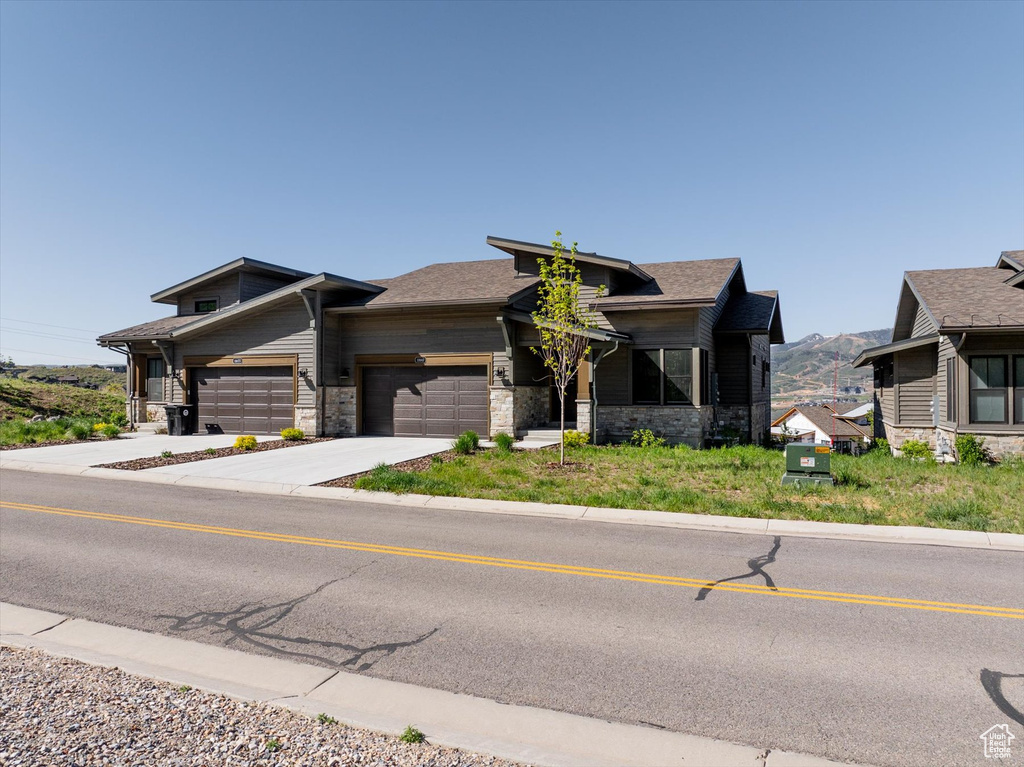 View of front of house featuring stone siding, a garage, concrete driveway, and a mountain view