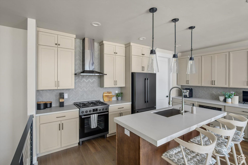 Kitchen featuring wall chimney exhaust hood, high end refrigerator, a sink, gas range, and tasteful backsplash