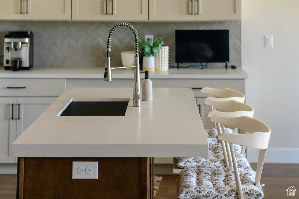 Kitchen with a sink, wood finished floors, decorative backsplash, light countertops, and baseboards