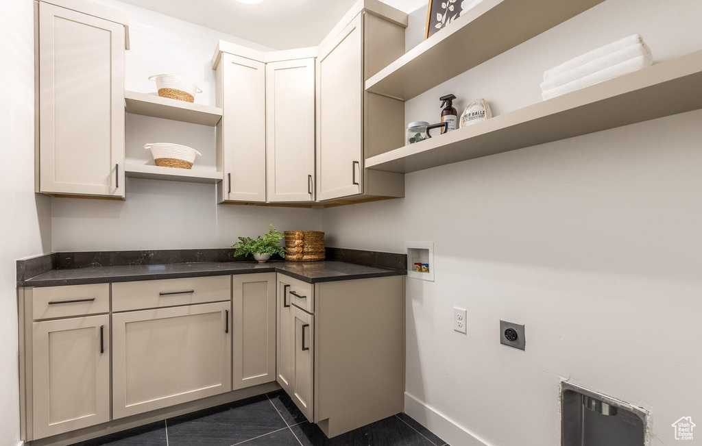 Washroom with electric dryer hookup, dark tile patterned floors, cabinet space, washer hookup, and baseboards