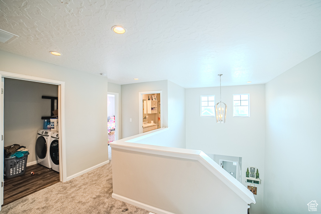 Corridor with washing machine and dryer, light carpet, an upstairs landing, baseboards, and a textured ceiling