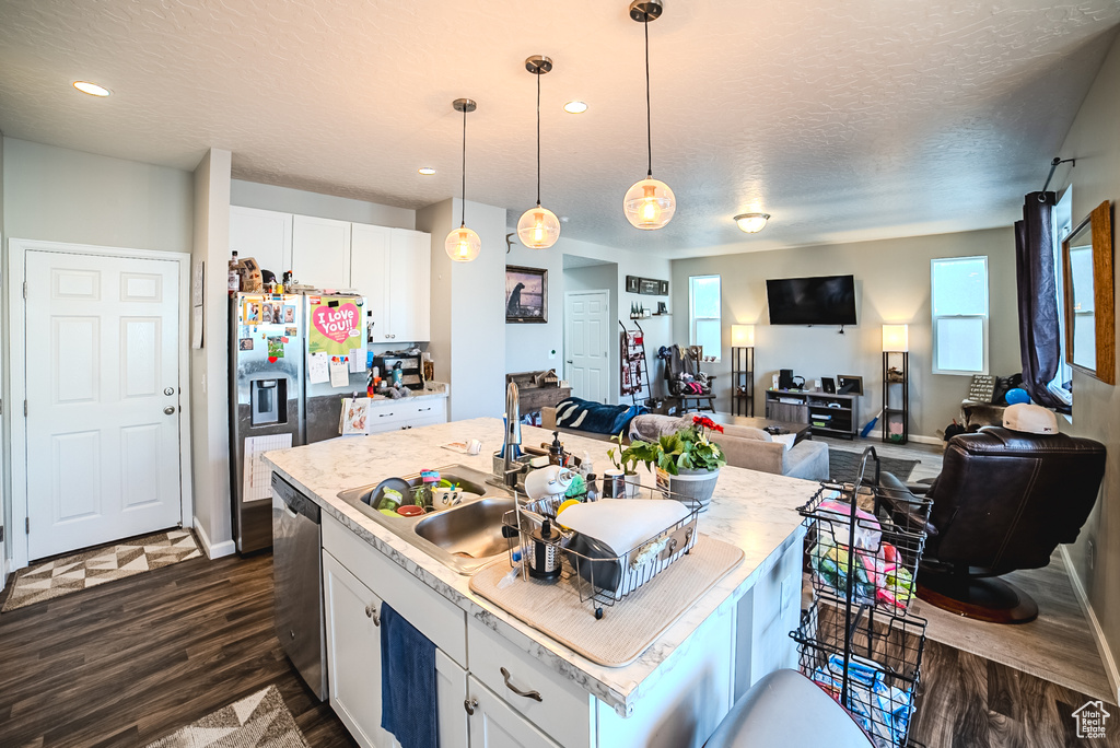 Kitchen featuring white cabinets, dark wood-type flooring, light countertops, a kitchen island with sink, and open floor plan