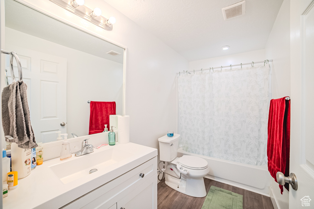 Bathroom featuring wood finished floors, vanity, toilet, and shower / bathtub combination with curtain