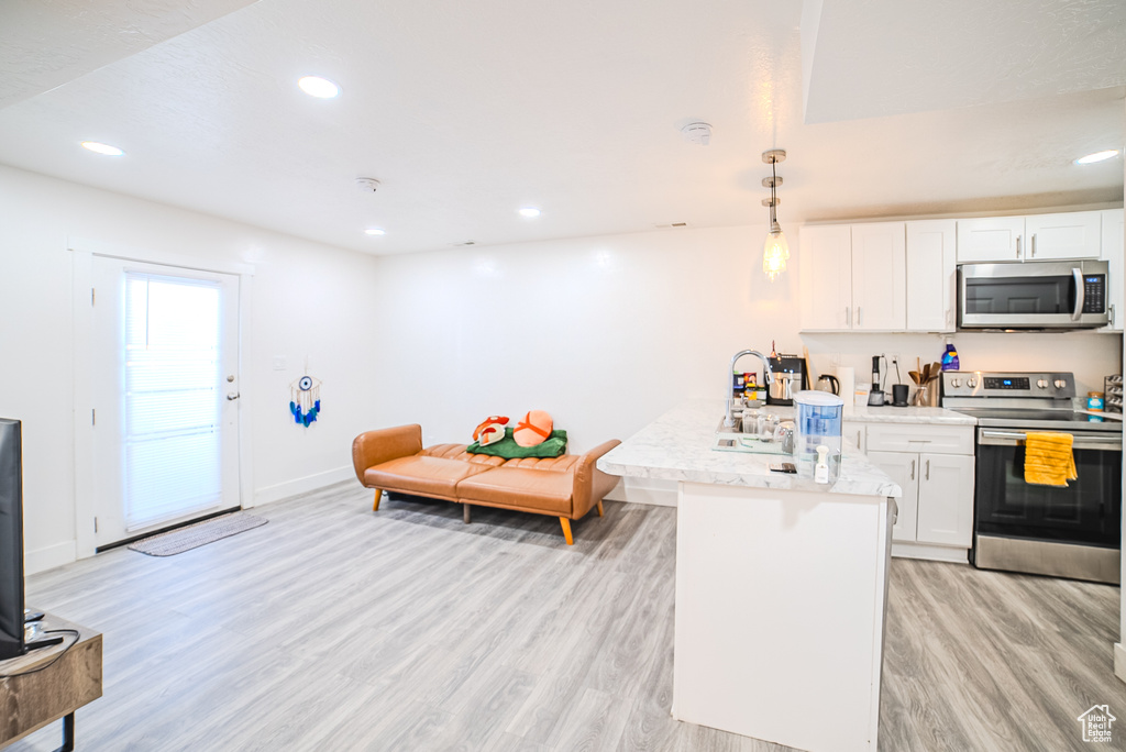 Kitchen with stainless steel appliances, light wood finished floors, white cabinets, a peninsula, and baseboards