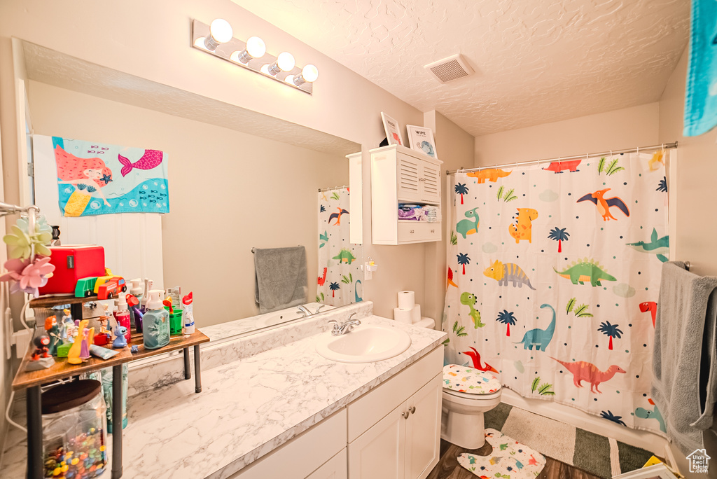 Full bathroom featuring toilet, vanity, a textured ceiling, and curtained shower