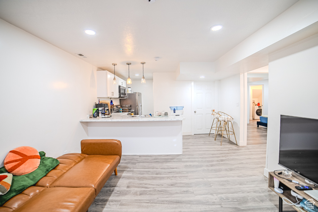 Kitchen with stainless steel appliances, light wood-style floors, white cabinetry, light countertops, and a peninsula