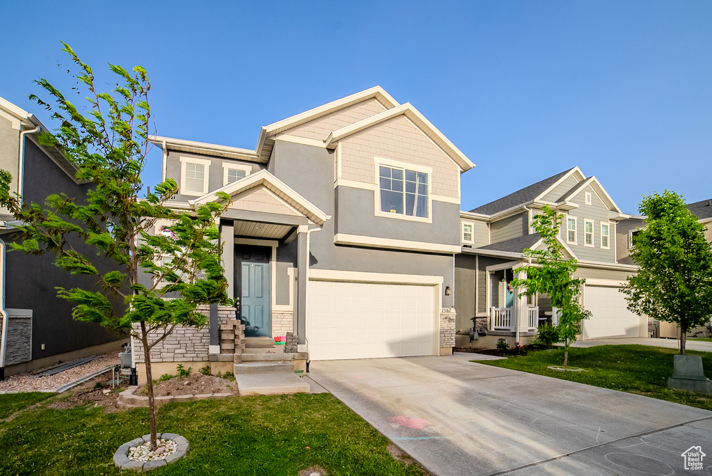 Craftsman inspired home featuring a garage, driveway, stucco siding, and a front lawn
