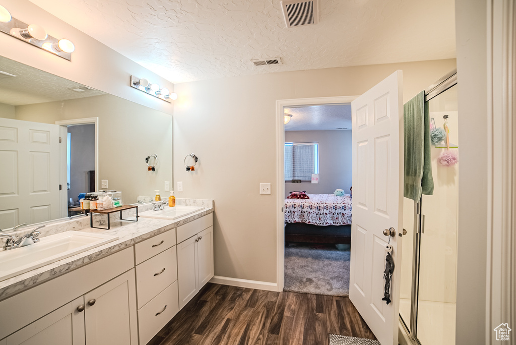 Ensuite bathroom with wood finished floors, double vanity, baseboards, a textured ceiling, and a stall shower