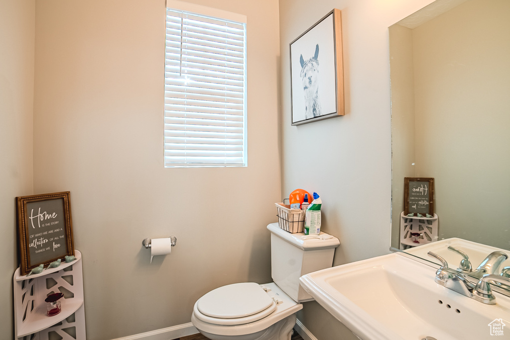 Half bath with toilet, a sink, plenty of natural light, and baseboards