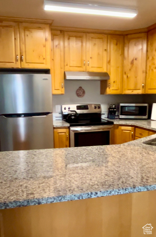 Kitchen featuring appliances with stainless steel finishes, under cabinet range hood, and light stone countertops