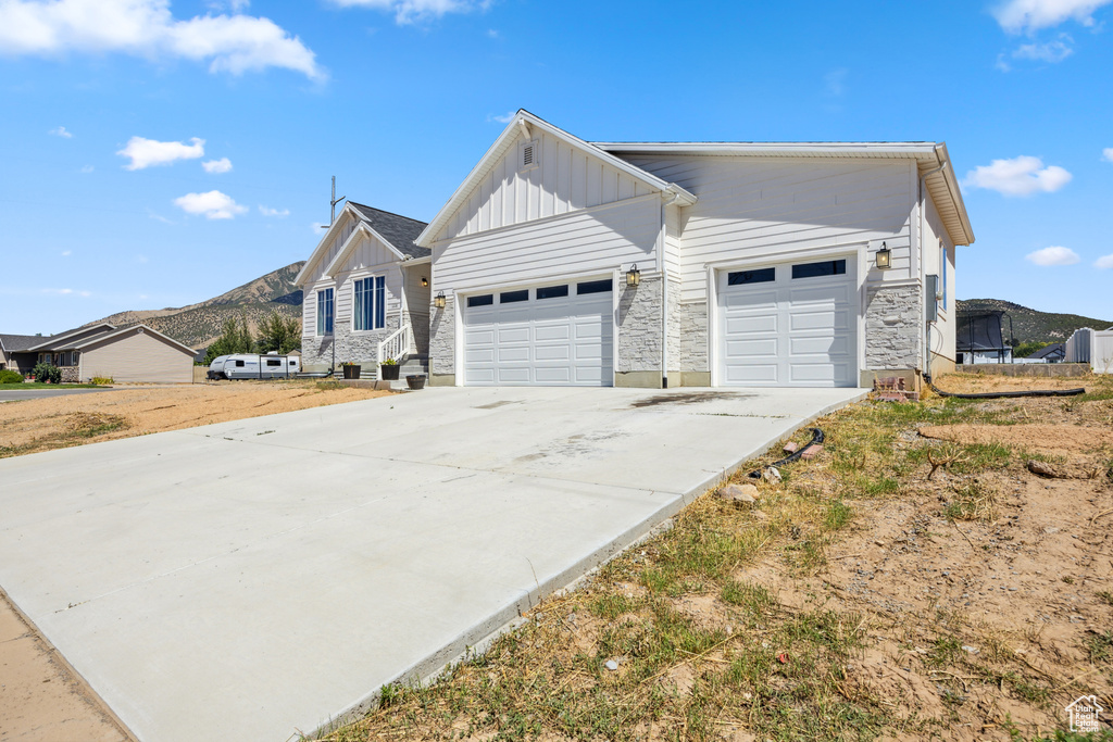 View of front of house featuring board and batten siding, a mountain view, an attached garage, concrete driveway, and stone siding
