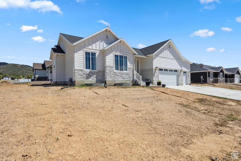 Modern farmhouse with board and batten siding, stone siding, a garage, and driveway