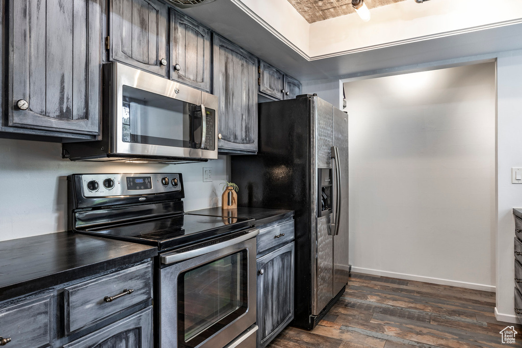 Kitchen with appliances with stainless steel finishes, dark countertops, dark wood finished floors, and baseboards