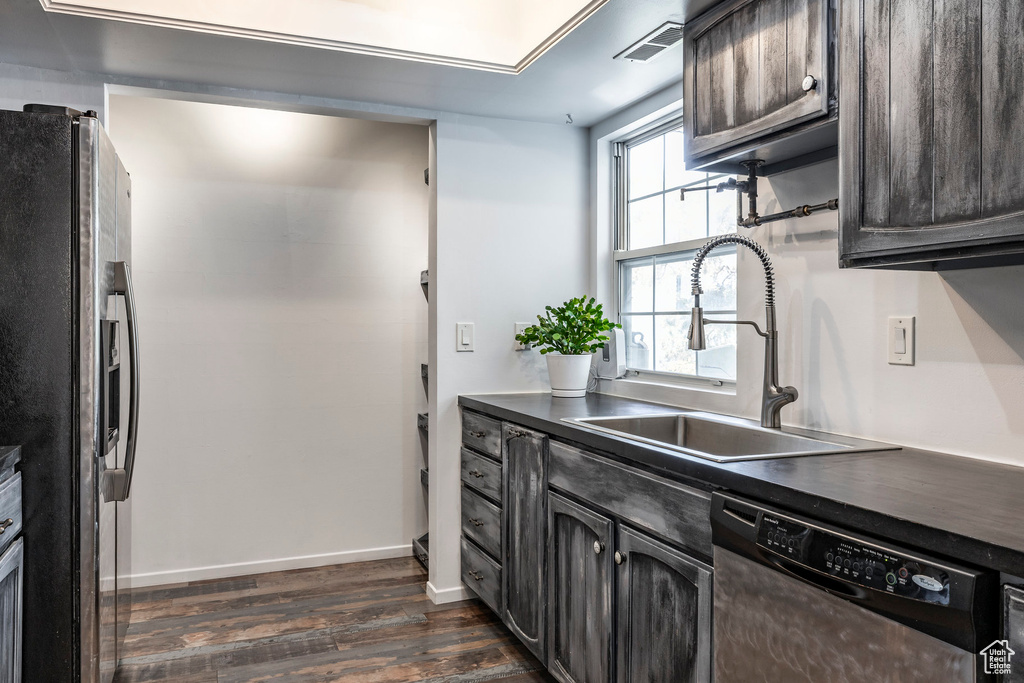 Kitchen with appliances with stainless steel finishes, a sink, dark wood finished floors, dark countertops, and baseboards