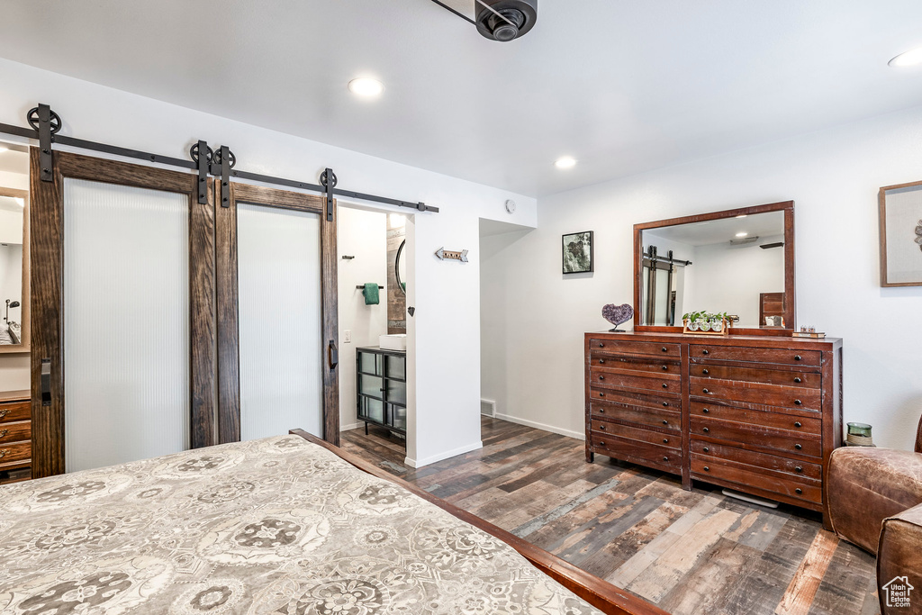 Bedroom with a barn door, wood finished floors, recessed lighting, baseboards, and connected bathroom