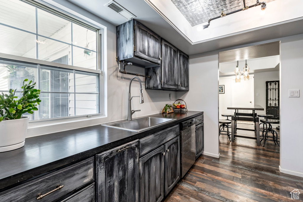 Kitchen featuring a sink, dishwasher, dark countertops, dark wood-style floors, and a tray ceiling
