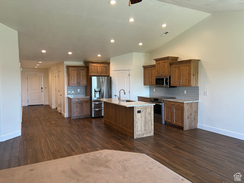 Kitchen with appliances with stainless steel finishes, a sink, baseboards, dark wood-style flooring, and lofted ceiling