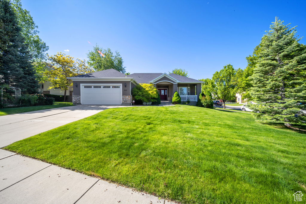 View of front of house featuring an attached garage, concrete driveway, a front yard, a porch, and stone siding