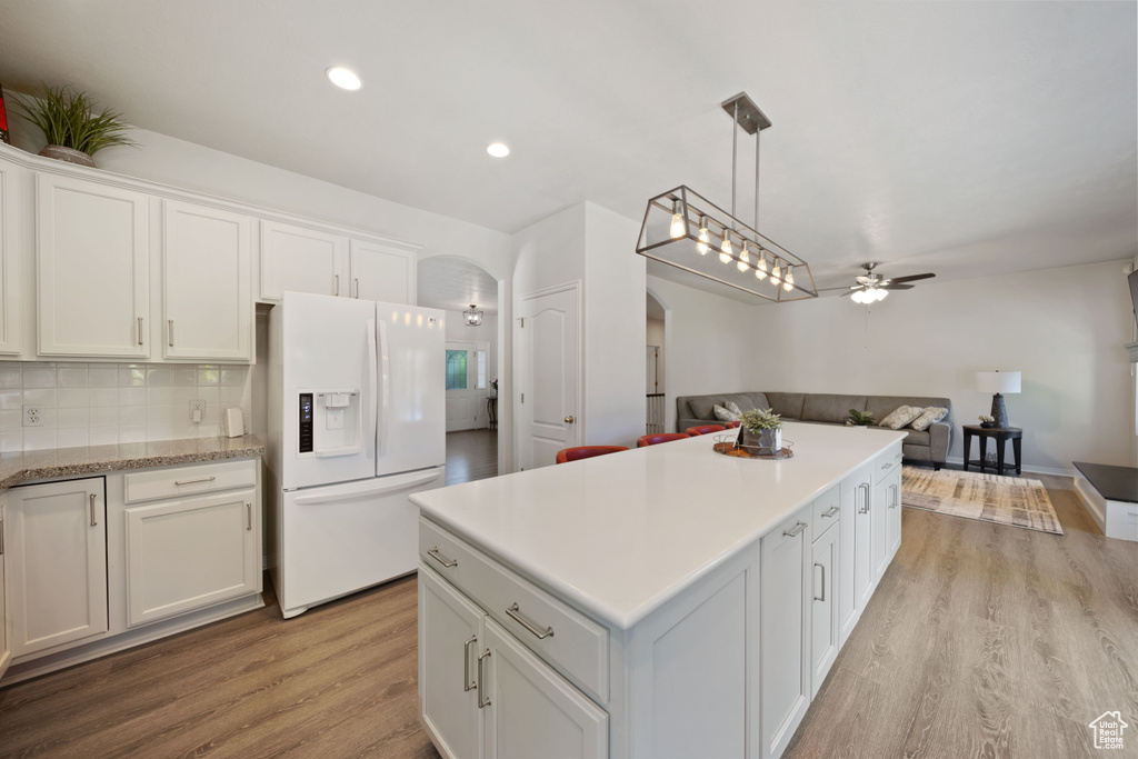 Kitchen featuring white refrigerator with ice dispenser, arched walkways, ceiling fan, a kitchen island, and light wood-style floors