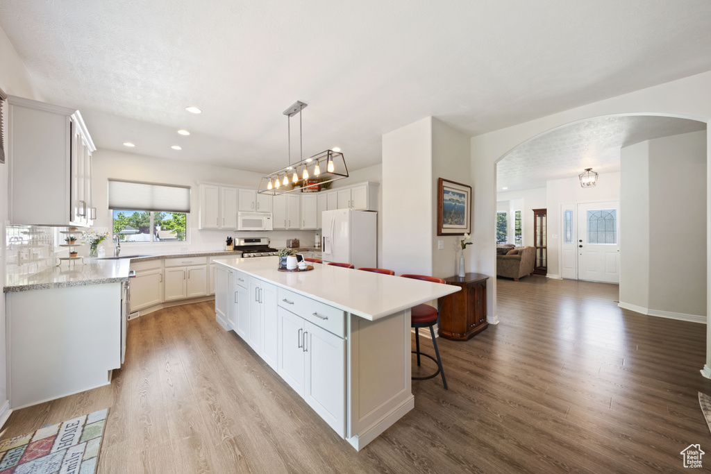 Kitchen featuring white appliances, arched walkways, a center island, light countertops, and recessed lighting
