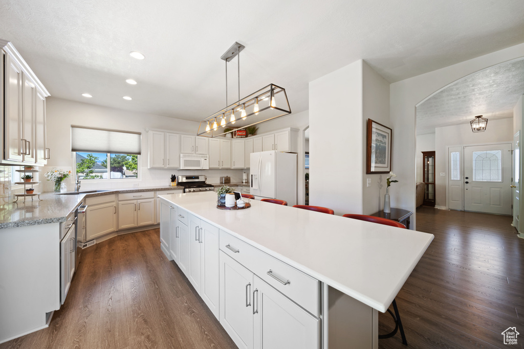 Kitchen with white appliances, light countertops, a kitchen island, recessed lighting, and dark wood-type flooring