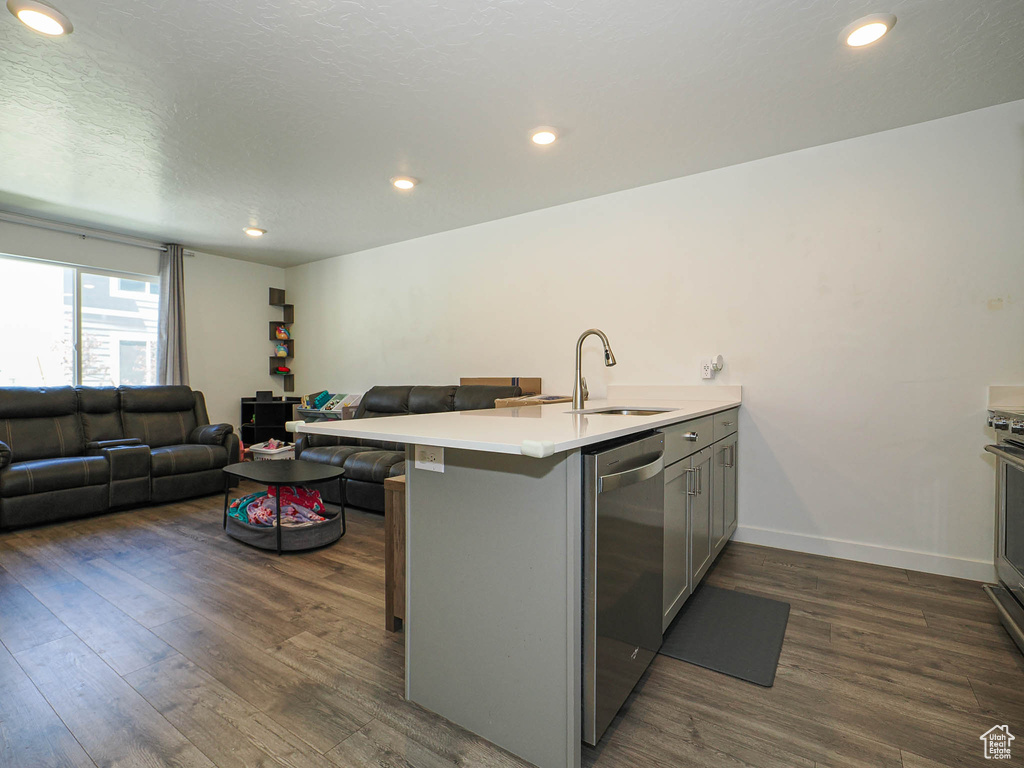 Kitchen with a sink, stainless steel dishwasher, open floor plan, dark wood finished floors, and a peninsula