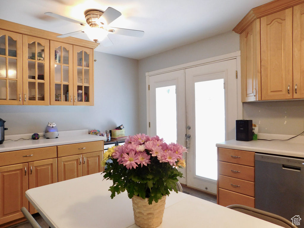 Kitchen with stainless steel dishwasher, light countertops, light brown cabinetry, and glass insert cabinets