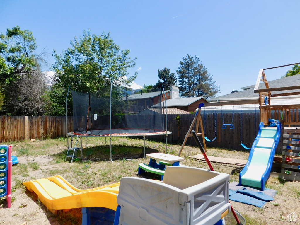 Fenced backyard featuring a trampoline and a playground