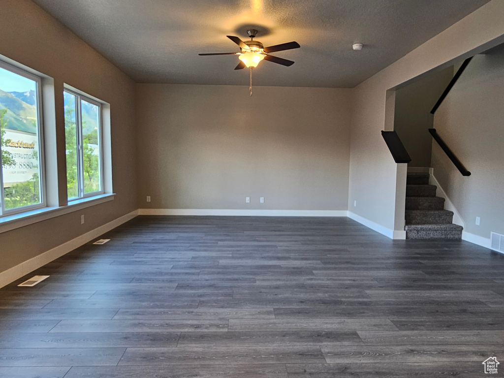 Unfurnished living room featuring stairway, dark wood-style flooring, a ceiling fan, and baseboards