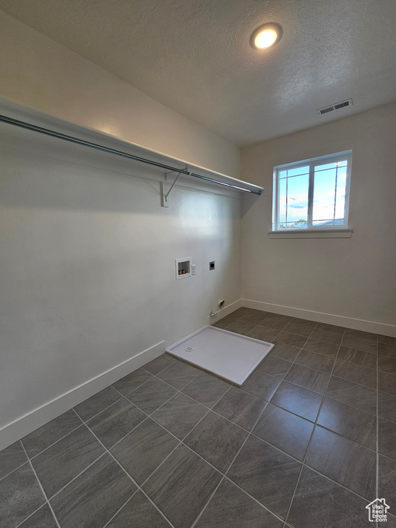 Laundry room with electric dryer hookup, hookup for a washing machine, dark tile patterned flooring, a textured ceiling, and baseboards