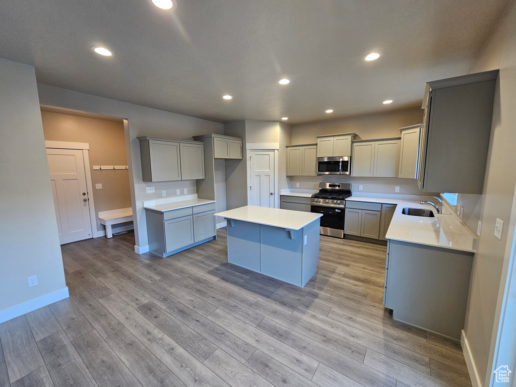 Kitchen with appliances with stainless steel finishes, a sink, a kitchen island, gray cabinets, and baseboards