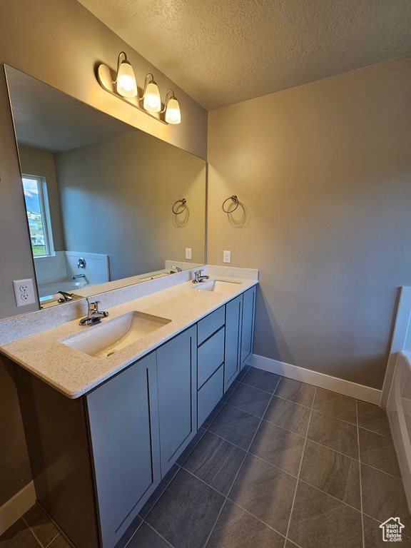 Full bath with double vanity, a textured ceiling, tile patterned floors, and baseboards