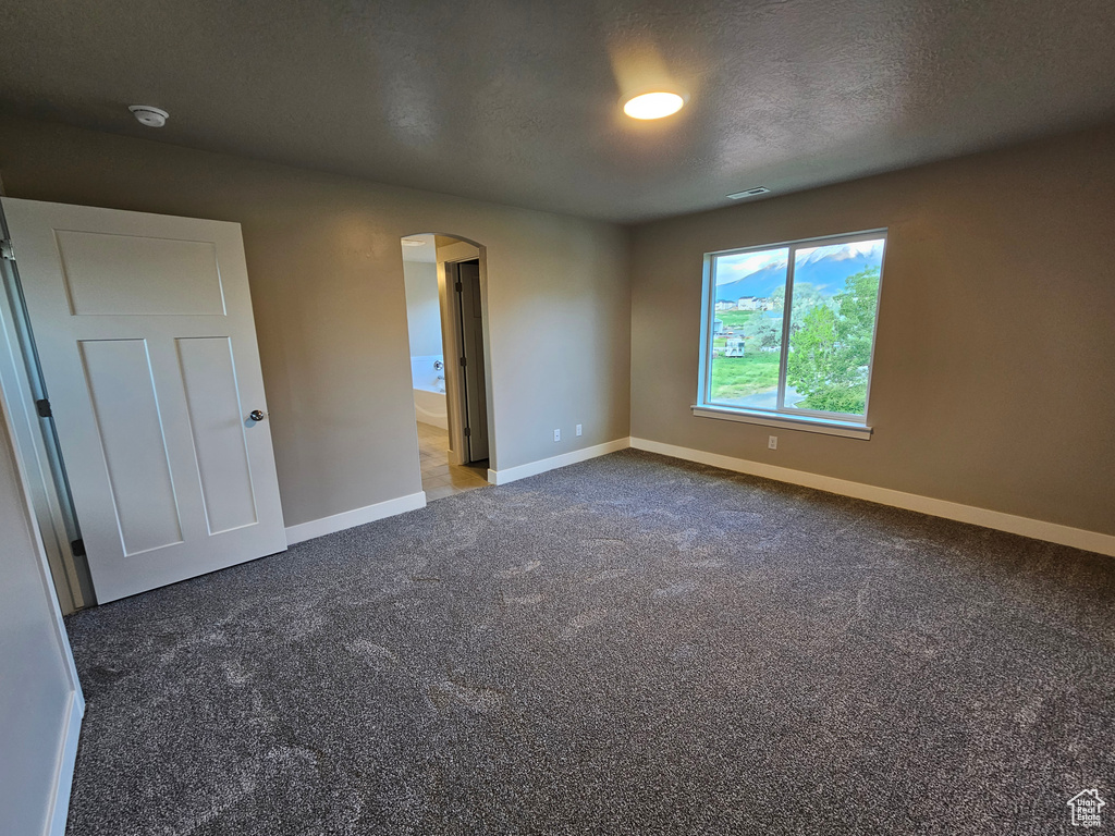 Unfurnished room featuring arched walkways, baseboards, carpet, a smoke detector, and a textured ceiling