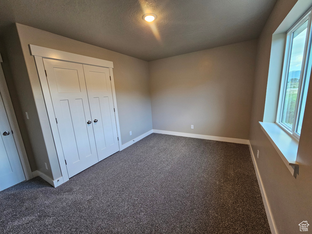Unfurnished bedroom featuring baseboards, dark colored carpet, a closet, and a textured ceiling