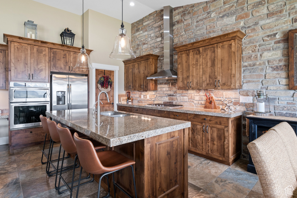Kitchen with stainless steel appliances, wall chimney range hood, a sink, tasteful backsplash, and a kitchen breakfast bar