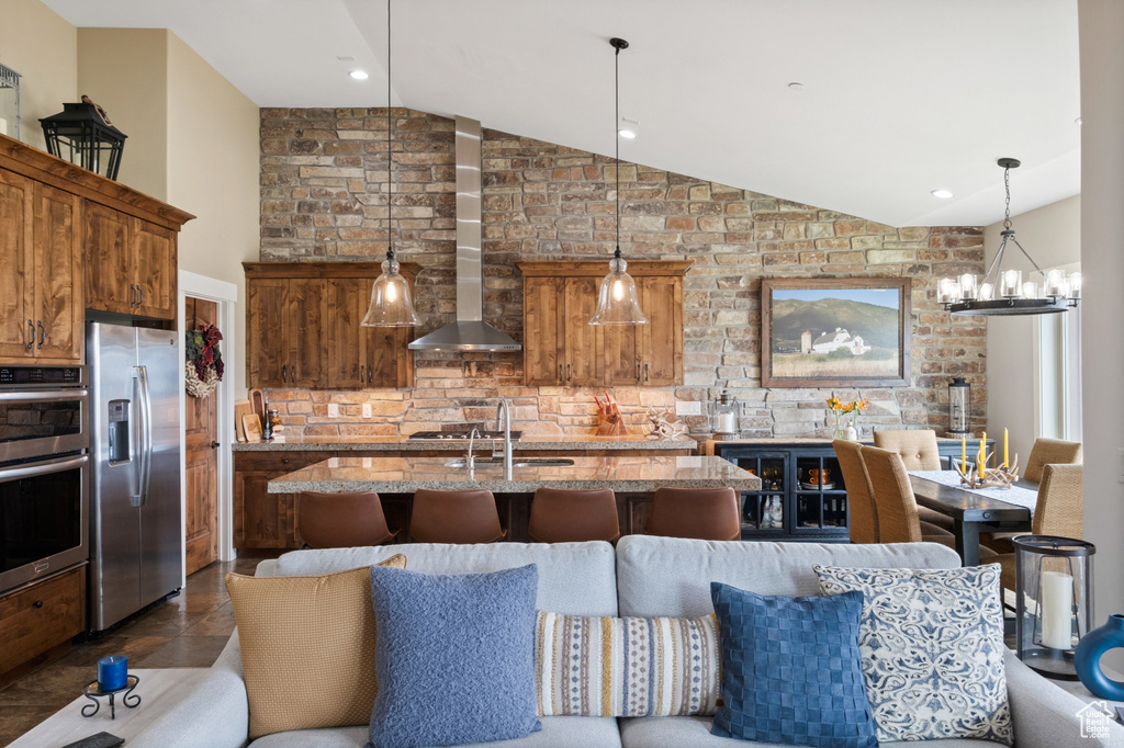 Kitchen featuring stainless steel appliances, lofted ceiling, wall chimney exhaust hood, an island with sink, and a sink