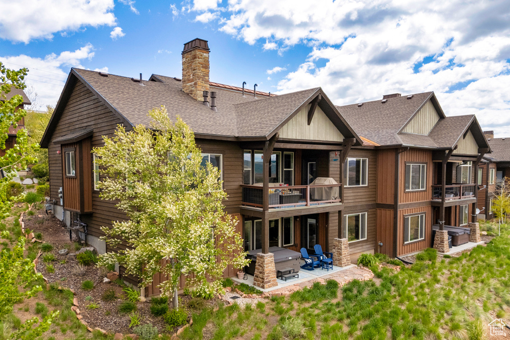 Back of house with a balcony, a patio area, a shingled roof, and a chimney