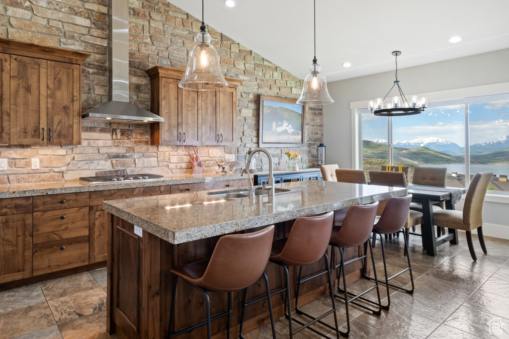 Kitchen with wall chimney exhaust hood, a sink, stainless steel gas cooktop, a kitchen island with sink, and backsplash