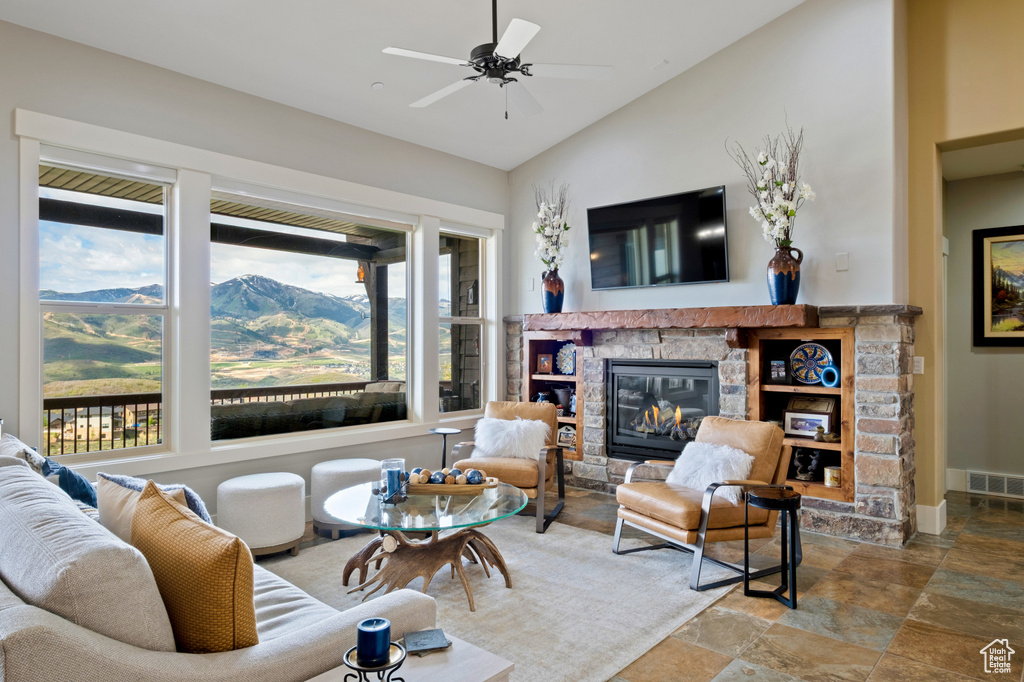 Living area featuring a stone fireplace, lofted ceiling, stone finish flooring, a ceiling fan, and baseboards